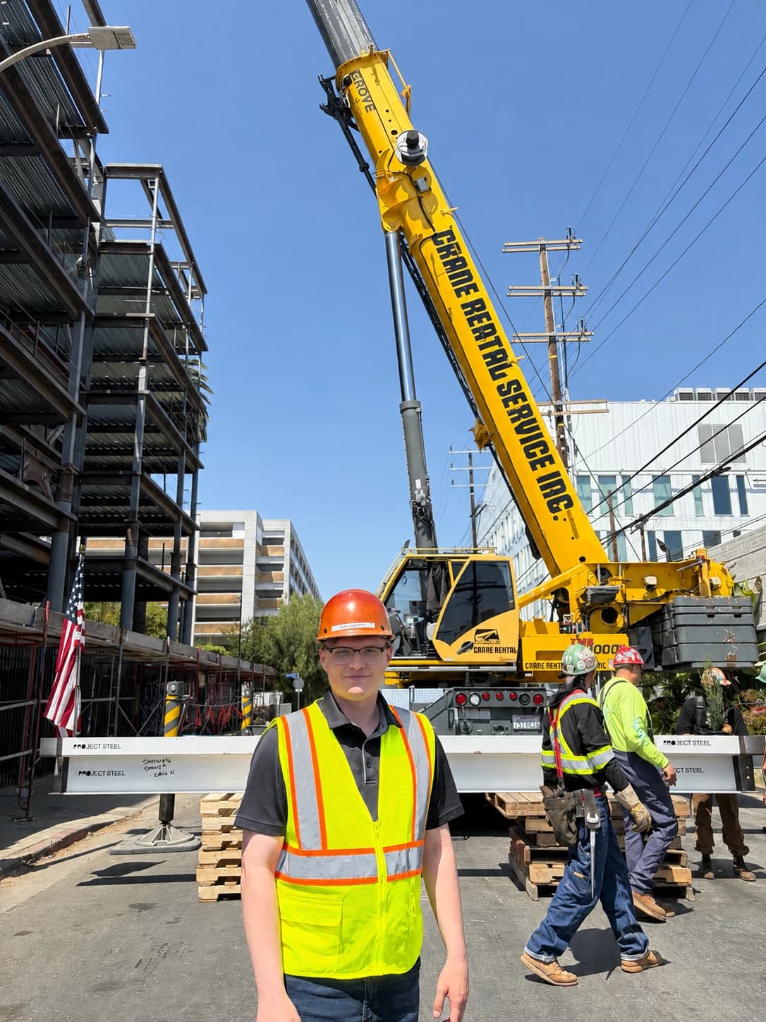 Kyle Langford wearing a hard hat and safety vest beside a crane and steel frame